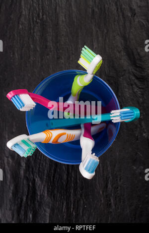 Toothbrushes in a blue plastic glass on black stone background Stock Photo
