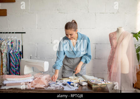 Professional female dressmaker choosing spool for clothes sewing on her desktop with tailoring accessories. Handmade work. Feminine hobby. Stock Photo