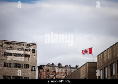 Canadian flag waiving in front of an old industrial zone made of abandoned silos, factories and warehouses on Montreal port, Quebec, Canada, closed a  Stock Photo