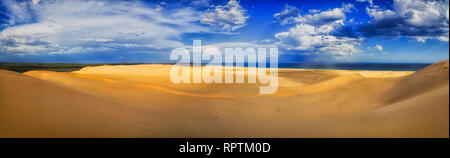 Bright clean sandy arid desert of sand dunes in Stockton beach under blue sky with clouds as wide panorama from Pacific ocean to gum-tree woods. Stock Photo