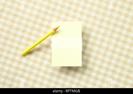 Yellow memo note pad and yellow colored pencil on beige check pattern fabric background Stock Photo