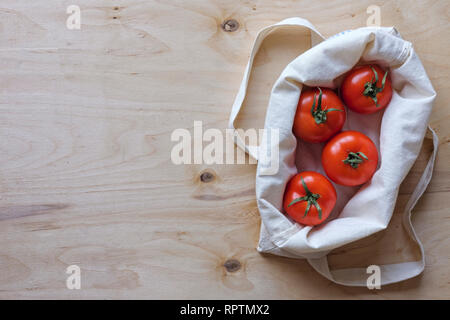 Overhead view of ripe tomatoes in a fabric bag arranged to the side on a wood background with copy space Stock Photo