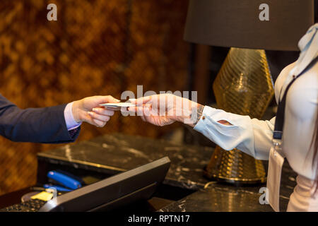 Close up of female hands with blank white badge arriving to hotel, gives credit card to female receptionist, checking in the hotel. Stock Photo