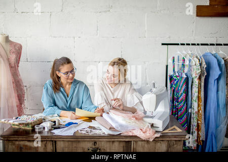 Cute blonde woman preparing to become a bride is looking sketches of popular skillful female fashion designer, being satisfied by well-done work, smil Stock Photo