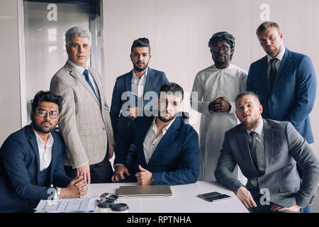 Diverse serious business men gather at conference table together with his caucasian athletic young boss, attending meeting or corporate briefing. Afri Stock Photo