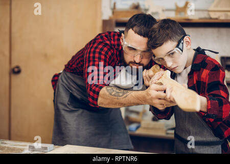 Little male woodworker creating his dream and his Dad is helping him.Close-up of young male carpenter examines with his son smoothness of DIY wooden s Stock Photo