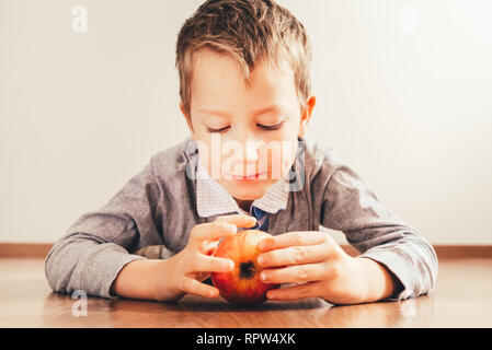 Boy lying down biting an apple, isolating white background, concept of healthy nutrition at home. Stock Photo