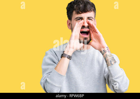 Young handsome man wearing sweatshirt over isolated background Shouting angry out loud with hands over mouth Stock Photo