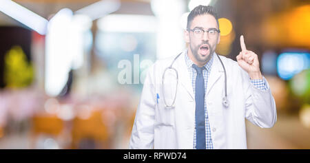 Handsome young doctor man over isolated background pointing finger up with successful idea. Exited and happy. Number one. Stock Photo