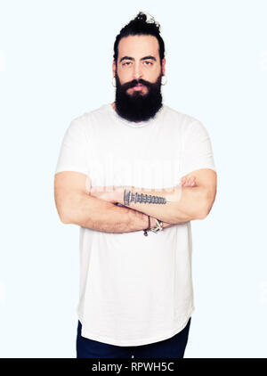 Young hipster man with long hair and beard wearing casual white t-shirt skeptic and nervous, disapproving expression on face with crossed arms. Negati Stock Photo