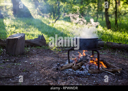 Over the fire hangs a pot in which to cook food. On a hook on a tripod,  steam comes out of the pan. Winter Camping outdoor cooking Stock Photo -  Alamy