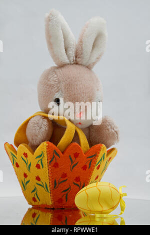 A plush toy bunny sitting in an Easter basket with yellow Easter egg Stock Photo