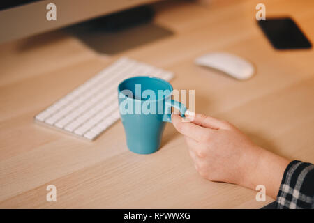 Coffee mug on a wooden table in front of the computer screen. Concept of a home office. Stock Photo