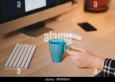 Coffee mug on a wooden table in front of the computer screen. Concept of a home office. Stock Photo