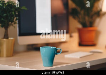 Coffee mug on a wooden table in front of the computer screen. Concept of a home office. Stock Photo