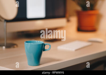 Coffee mug on a wooden table in front of the computer screen. Concept of a home office. Stock Photo