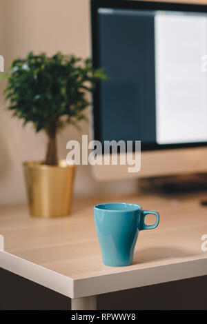 Coffee mug on a wooden table in front of the computer screen. Concept of a home office. Stock Photo