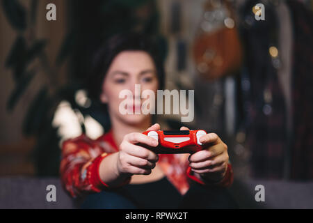 Beautiful young woman having fun playing video games in her free time. Focus on the gaming controller. Stock Photo