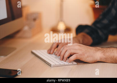 Top view close up of male hands using a wireless keyboard, set on a wooden working table. Stock Photo