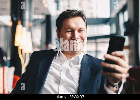Close-up of attractive young man having a video call in a cafe bar during a break from work, smiling and looking at the camera on his smartphone. Stock Photo