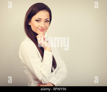 Beautiful business calm confident woman in white looking with hand under the face on toned color  background. Bank style employee Stock Photo