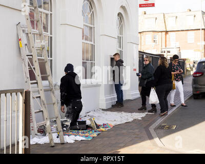 Painter painting local post office whilst people use ATM, Bude, Cornwall, UK Stock Photo