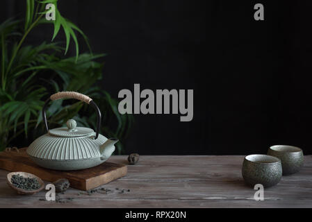 Teapot and Teacups on black background, copy space. Traditional Asian arrangement  for Tea ceremony -  iron teapot and ceramic teacups with tea. Stock Photo