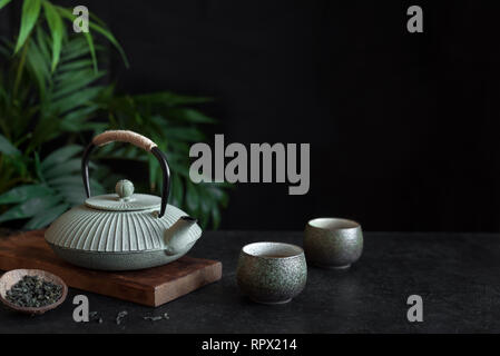 Teapot and Teacups on black background, copy space. Traditional Asian arrangement  for Tea ceremony -  iron teapot and ceramic teacups with tea. Stock Photo