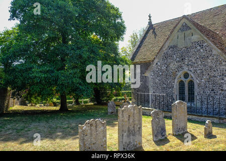 Jevington, Sussex, UK - August 1, 2018: side view of St. Andrew's church in Jevington with old grave stones and large tree.  Ancient flint built churc Stock Photo