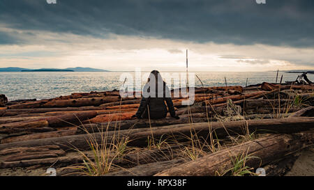 Woman sitting on rocks looking out to sea, British Columbia, Canada Stock Photo