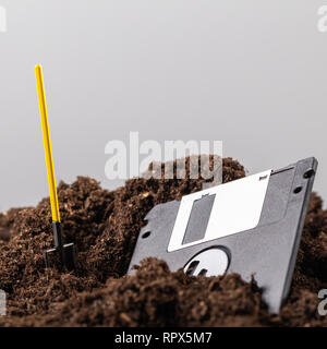 The diskette is half buried in the ground, next to a shovel Stock Photo