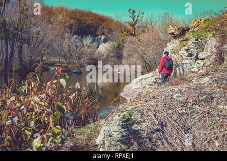 A tourist stands on a rocky shore of the mountain river in the canyon on a sunny autumn day. The man looks at the river