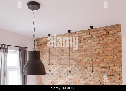 Modern black metallic lamp and three of retro bulbs in room with old brick wall Stock Photo