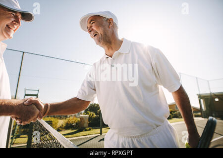 Two cheerful senior tennis players shaking hands on tennis court. Happy tennis players greeting each other after a game of tennis. Stock Photo