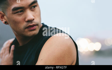 Close up shot of fit young man with muscular build standing outside and looking away. Asian fitness model looking away and thinking. Stock Photo