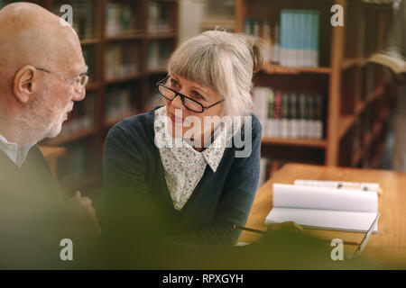 Senior man and woman discussing subject sitting in a university classroom. Close up of an elderly couple sitting in a library and discussing with book Stock Photo