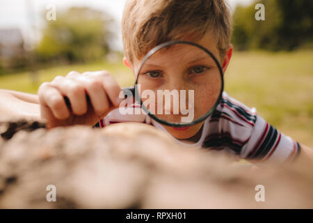 Closeup of cute kid with magnifying glass outdoors. Boy exploring with magnifying glass at the park. Stock Photo