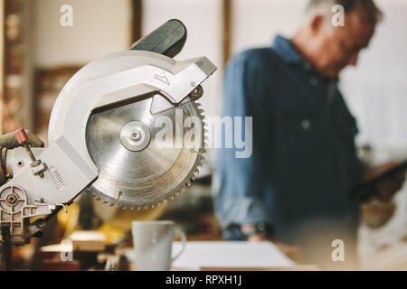 Circular wood saw in carpentry workshop with carpenter in background. Cutting tool in carpentry workshop. Stock Photo