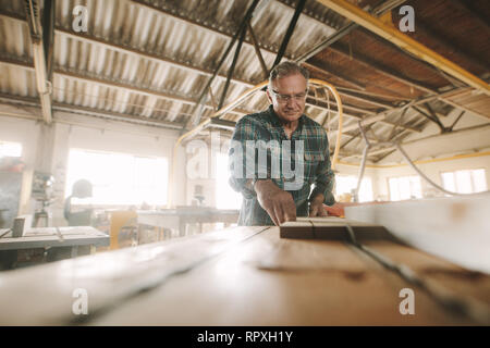 Senior carpenter works on the machine with the wooden product manufacturing. Carpenter cuts the wood of various configurations on the circular saw mac Stock Photo