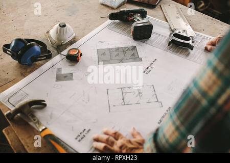 Carpenter reading a floor plan with his tools lying by. Building plan on bench with carpentry tools. Stock Photo