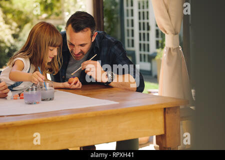 Man helping his daughter in painting easter eggs. Little girl holding an egg to paint it. Stock Photo