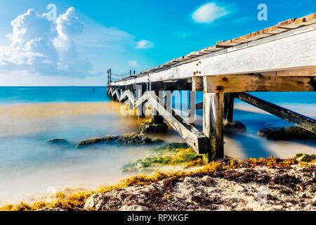 Calm scene of abandoned old rustic wooden jetty out to the sea during a tropical sunny day on the caribbean coast of Mexico. Stock Photo