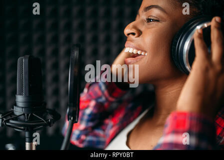 Female singer in headphones songs in audio recording studio. Musician listens composition, professional music Stock Photo