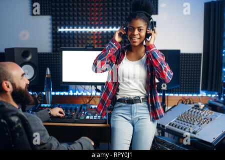 Sound producer and female performer in headphones listens composition in recording studio. Professional audio and music mixing technology Stock Photo