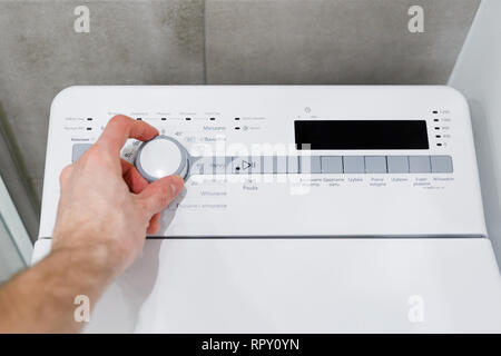 Men's hand sets up mode on upright washing machine Stock Photo