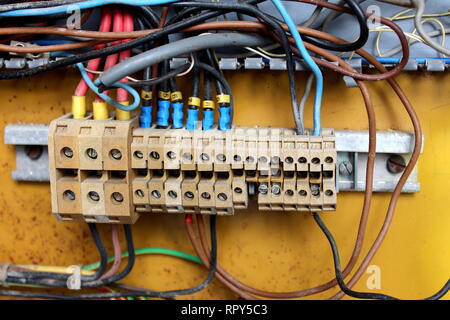 Multiple dirty insulated wires inside electrical box connected with ceramic electrical terminal connector strips in various sizes on warm sunny day Stock Photo
