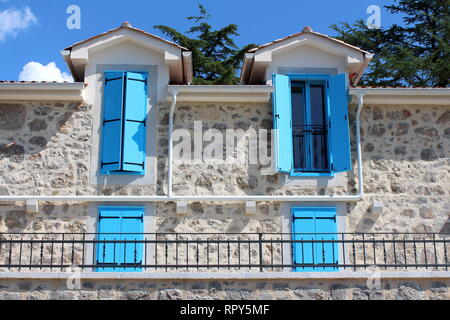 Open and closed light blue wooden window blinds on windows of newly built Mediterranean villa in traditional stone style with front balcony Stock Photo