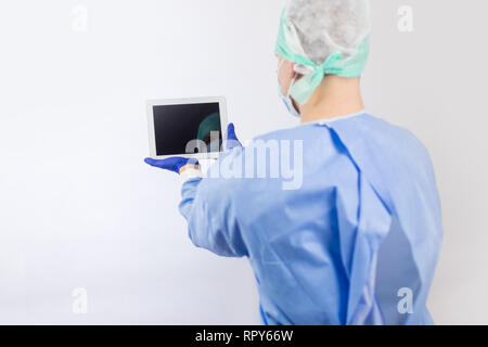 Surgeon doctor in sterile gloves preparing for operation using tablet computer. He is wearing surgical cap and blue gown Stock Photo