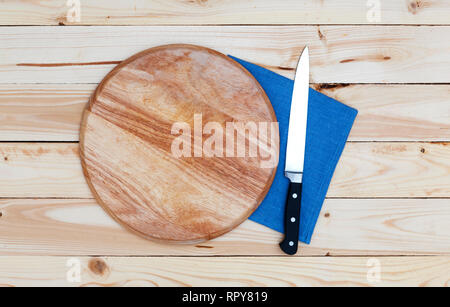 Round cutting board with a knife on a wooden table, top view Stock Photo