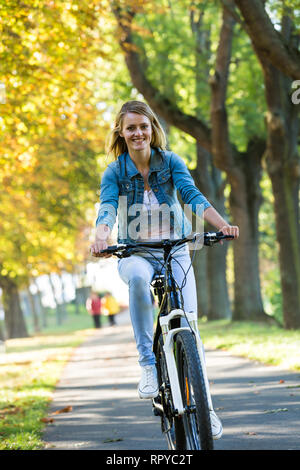 Young woman ride bike in autumn park. Enjoying while cycling in nature during autumn day. Stock Photo